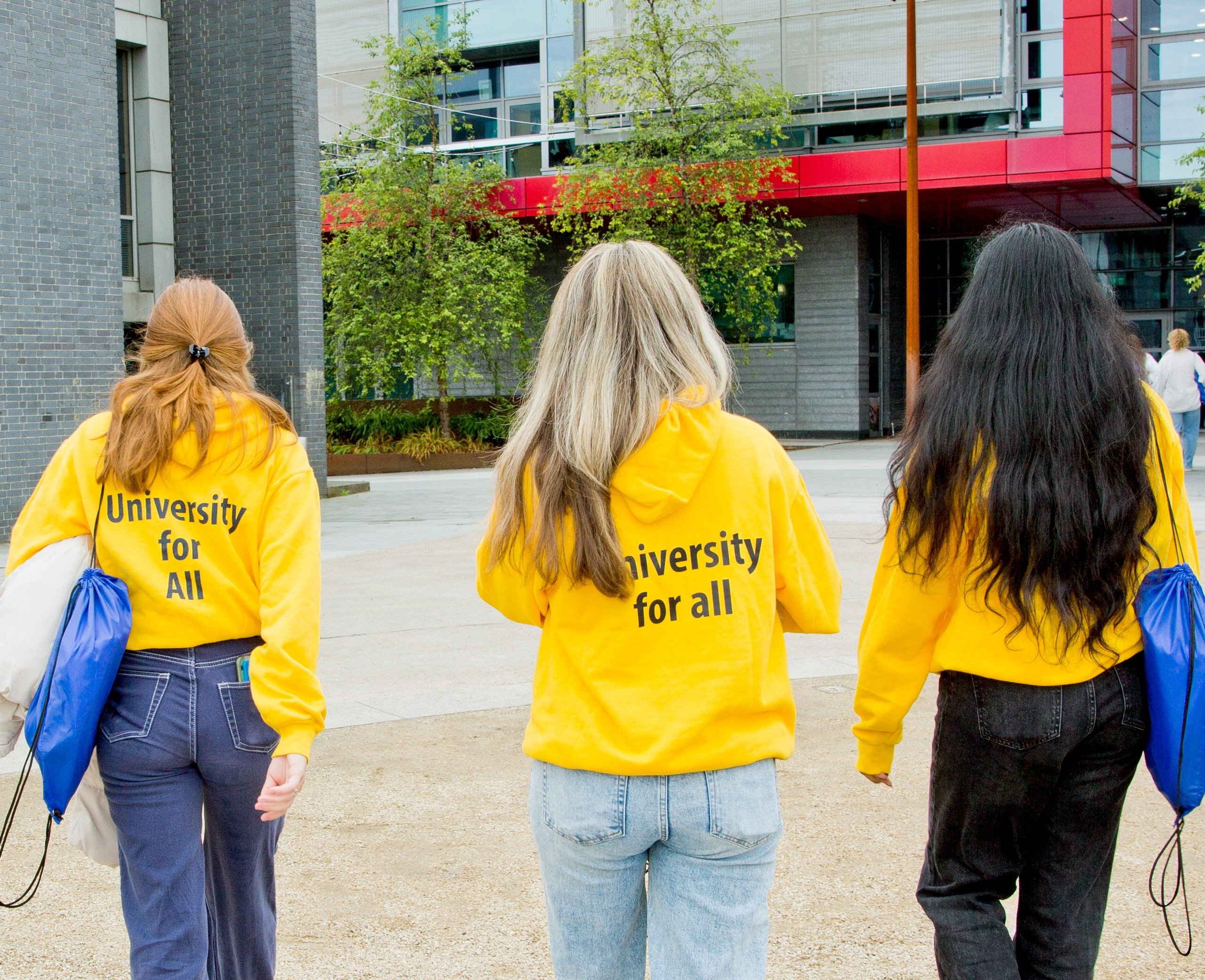 3 UCD students wearing university for all sweaters are walking on campus.