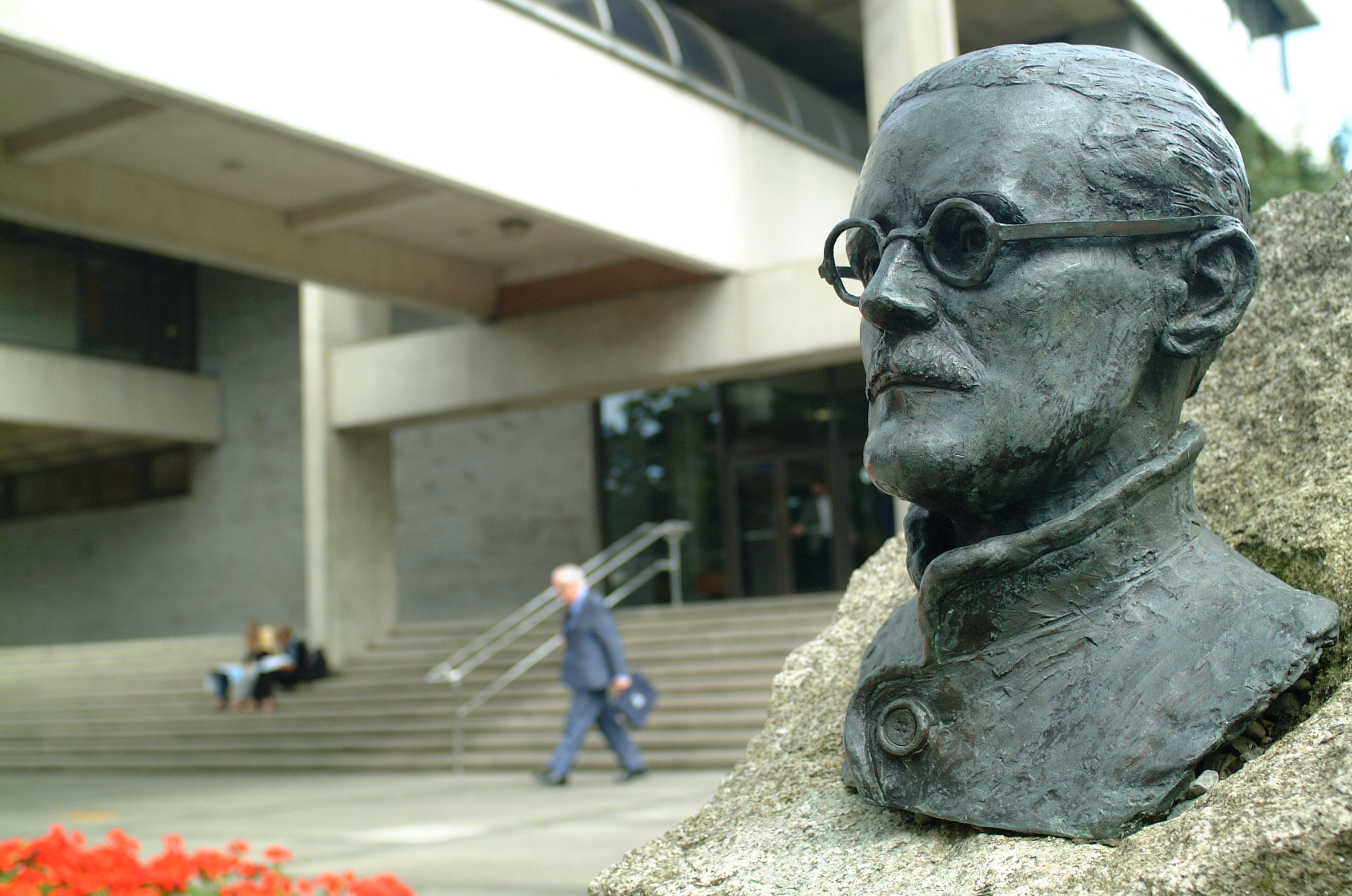 A bust of a man wearing glasses in front of a building's steps
