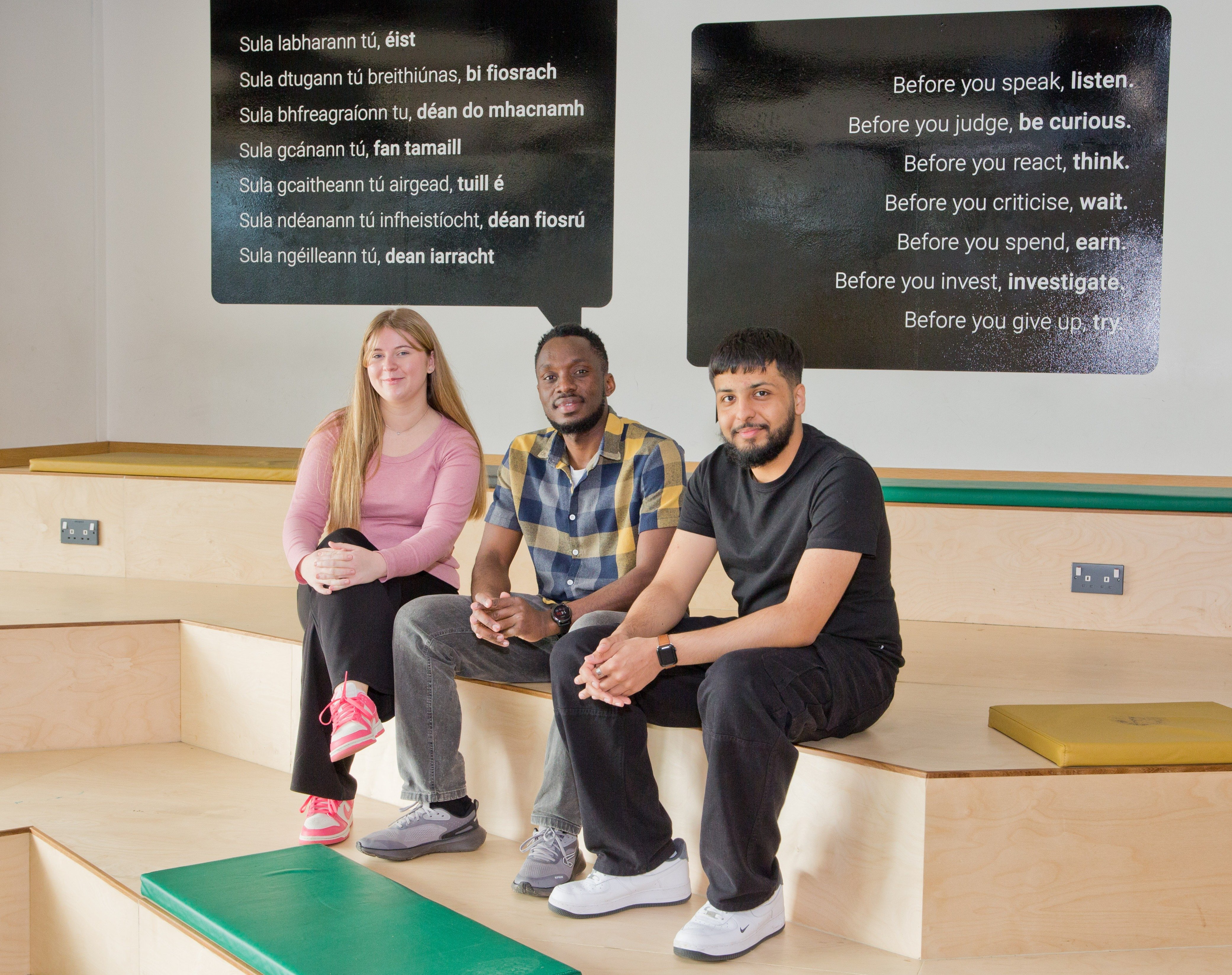 Three UCD students sitting on stairs, looking at the camera.