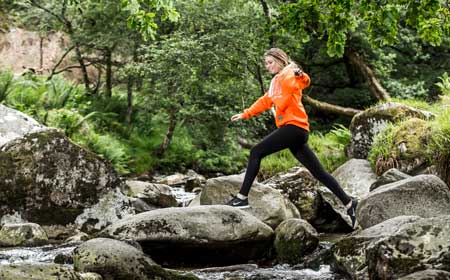 A woman in an orange hoodie crossing a stream