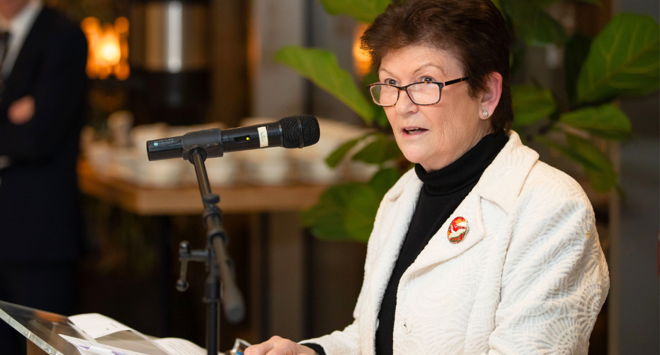 Woman with dark hair wearing a white jacket presenting at a podium