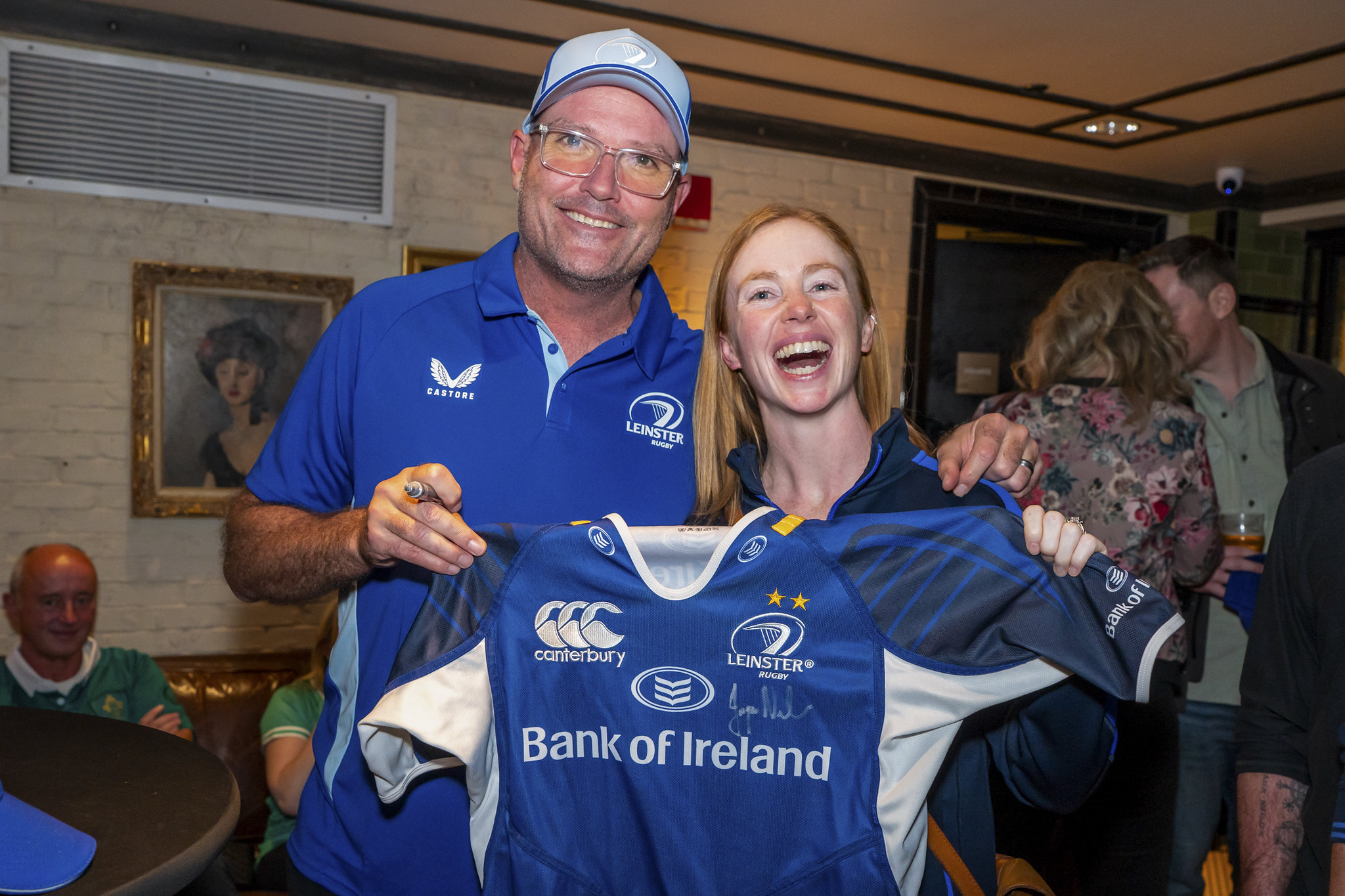 Leinster Rugby Coach standing with a UCD alumna, both smiling and holding a signed Leinster Rugby jersey.