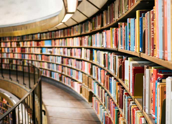 Curving library shelves packed with colourful books along a narrow walkway with a railing.