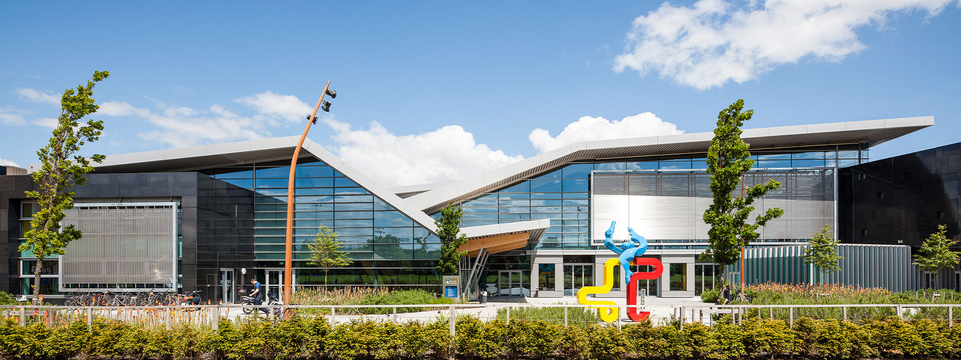 Colourful sculpture outside a large glass building.