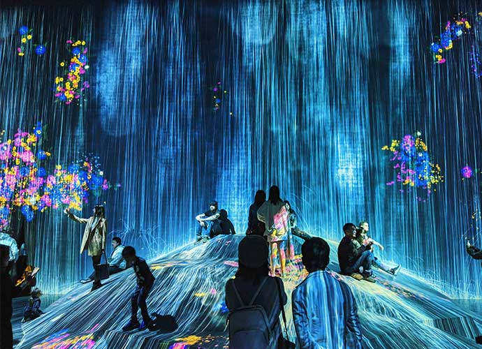 People interact with a digital art installation featuring cascading blue light projections and colourful flower-like visuals.