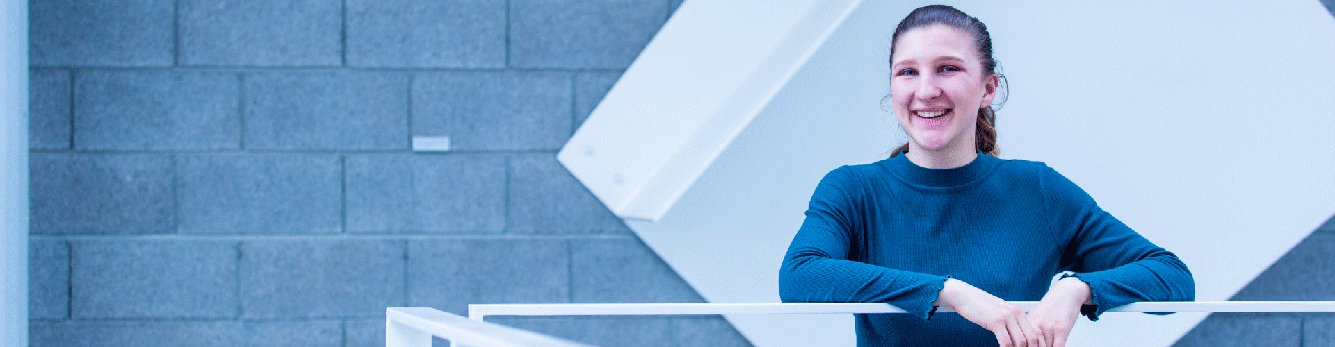 Female student in a blue shirt leans against a railing.