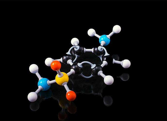 A colourful 3D molecular model with connected spheres representing atoms, displayed on a reflective black surface.