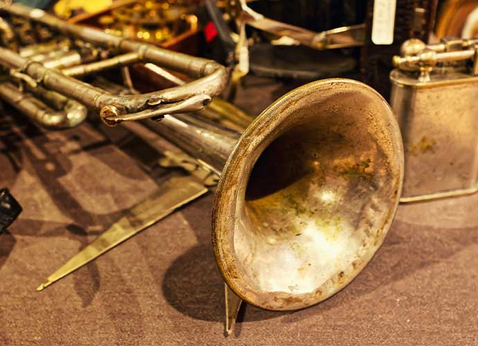 Close-up of an old, tarnished brass trumpet with a dented bell, lying on a table among other musical instruments.