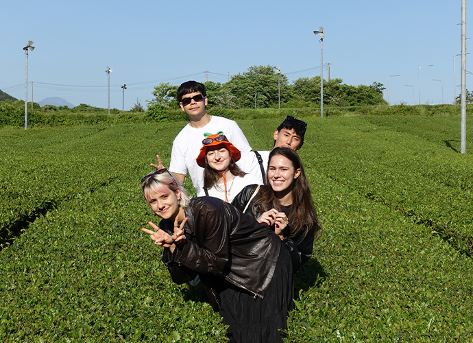 A group of five smiling students posing in a grassy field on a sunny, clear day.