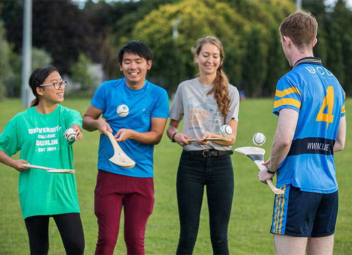 Four people standing on a grassy field practising hurling.