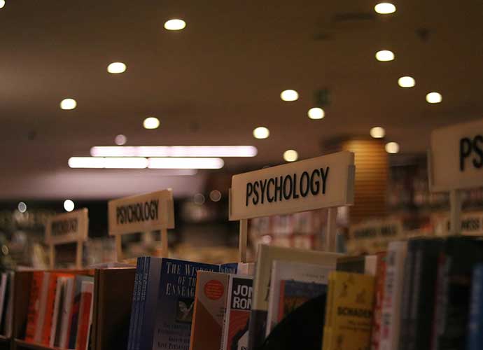 Bookshelves in a bookstore or library with section signs labelled “Psychology,” filled with books on the subject, under warm ceiling lights.