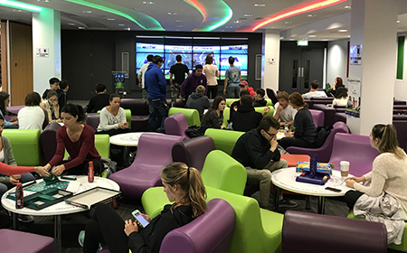 Students sitting around chatting in a large funky room full of comfy green and purple chairs.