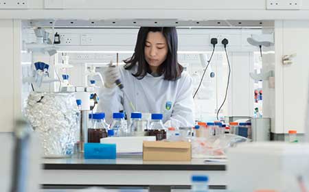Student in a lab coat working with equipment and samples in a university science laboratory.