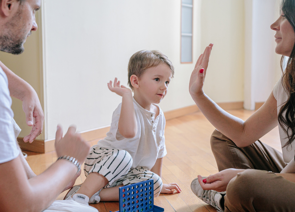 Child sitting on floor high fiving woman to the right with man to the left