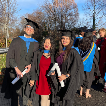 UCD graduates in caps and gowns outside on a sunny graduation day.