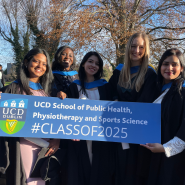 UCD graduates in caps and gowns holding a UCD sign.