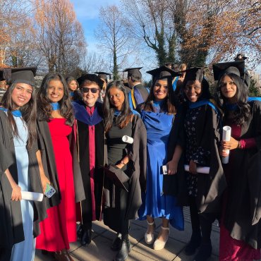 UCD graduates in caps and gowns outside on a sunny graduation day.
