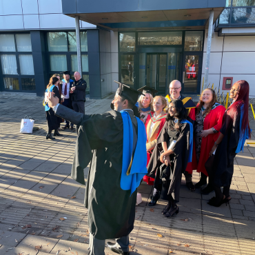 UCD graduates and UCD academic in caps and gowns outside on a sunny graduation day.