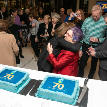 People hugging beside two cakes at the UCD Physiotherapy 70th anniversary celebration