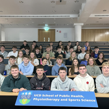 Group of students in a university lecture theatre holding a blue sign