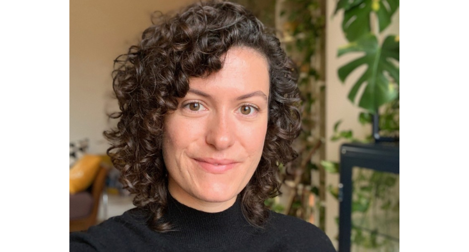 Woman with brown curly hair wearing a black top smiling to camera