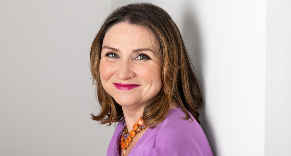 Woman with brown hair wearing a purple top smiling to camera
