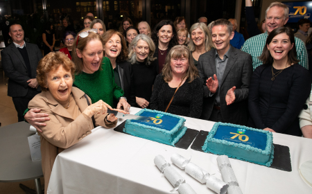 Woman cutting a cake surrounded by a group of people at the UCD Physiotherapy 70th anniversary celebration